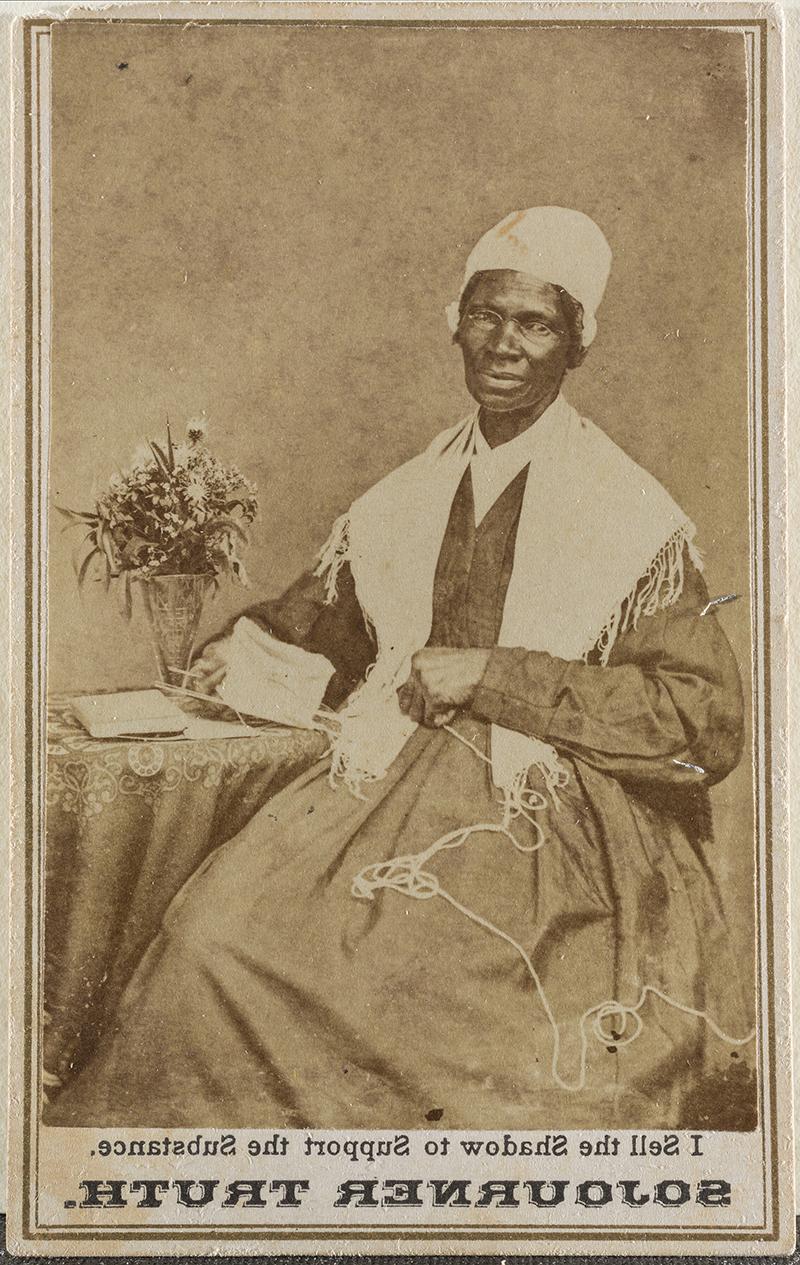 a sepia photograph showing a seated woman in a long dress with a shawl and cap